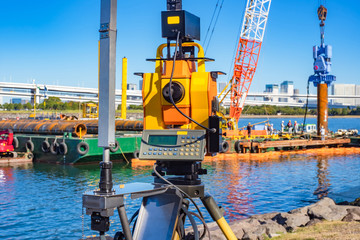 Theodolite on the background of the construction of the pier. Laser level for measuring angles of inclination. Theodolite helps in construction. Orange measuring device on a tripod.