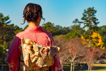 Fototapeta premium Japan. Geisha admires Nara Park. A girl in a kimono on the background of autumn trees. Autumn in Japan. National costume. Kimono. Japanese women's clothing. Natural attractions of Japan.