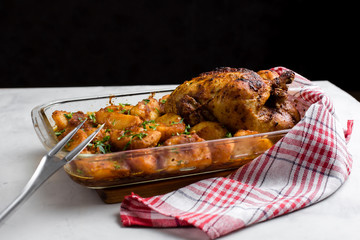 Baked whole chicken with potatoes and herbs in a rustic style. Top view, side view on a light background. Close-up and medium plan. Space for text.