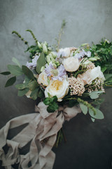 Bridal bouquet. The bride's bouquet. Beautiful bouquet of white, blue, pink flowers and greenery, decorated with long silk ribbon lies on a gray textural background