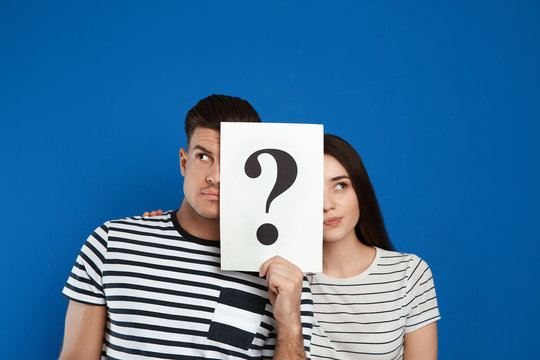 Couple holding question mark sign on blue background - Powered by Adobe