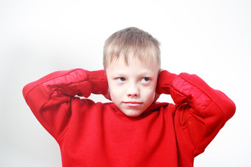 six-years old boy in red hoodie closing ears with his hands on grey background. Autism concept. Child does not want to hear. Protective pose, protectiveness, childhood traumatic experience.