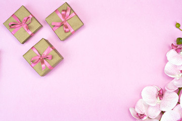 flat-lay of present gift boxes with pink ribbon on pink background with orchid flowers. spring concept. Copy space