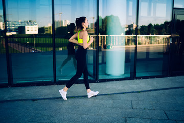 Fototapeta na wymiar Strong active female jogger in active outfit having morning training motivated with reaching goals, caucasian sportswoman with perfect body shape running on cardio workout having energy and motivation