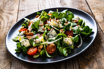 Fresh salad - blue cheese, cherry tomatoes, vegetables and walnuts on wooden background