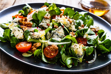 Fresh salad - blue cheese, cherry tomatoes, vegetables and walnuts on wooden background