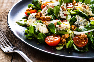 Fresh salad - blue cheese, cherry tomatoes, vegetables and walnuts on wooden background