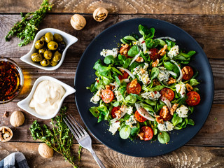 Fresh salad - blue cheese, cherry tomatoes, vegetables and walnuts on wooden background