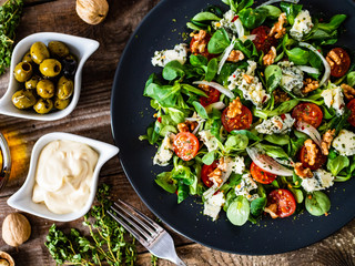 Fresh salad - blue cheese, cherry tomatoes, vegetables and walnuts on wooden background