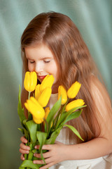 Portrait of a brunette child girl with bouquet of yellow tulips on a blue background
