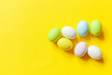 Happy Easter concept. Preparation for holiday. Easter candy chocolate eggs colorful pastel sweets and bunny toy isolated on trendy yellow background. Simple minimalism flat lay top view copy space