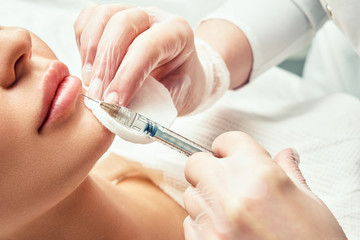 lip shape correction procedure in a cosmetology salon. The specialist makes an injection on the...