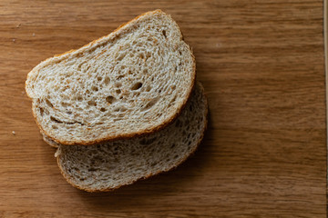 Two sliced slices of bran bread with a crisp crust of rye flour, lying on a brown wooden table,...