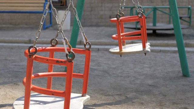 Empty swings on playground swaying in wind
