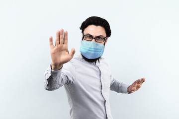 man in medical protective mask  standing and raising his palm doing the stop sign with a serious face on a gray background, stop coronavirus concept
