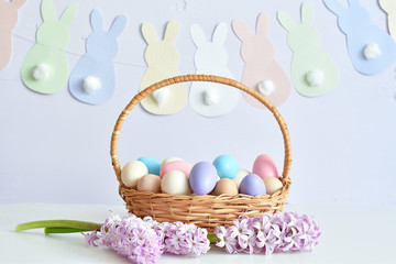 Colorful easter eggs in basket on pastel color background with flowers, copy space.Easter decorations. Easter background with painted eggs with Hyacinth, top view. Spring greeting card