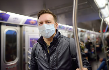 Mature man wearing disposable medical face mask in car of the subway in New York during coronavirus outbreak.