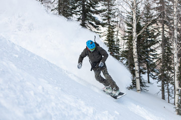 Fototapeta na wymiar A snowboarder making a powder turn in deep snow on a forest meadow on a sunny morning