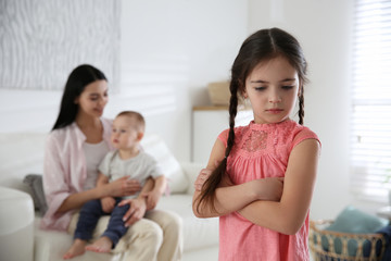 Unhappy little girl feeling jealous while mother spending time with her baby brother at home