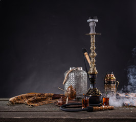 Fototapeta na wymiar Rustic handmade hookah and arabic tea for relaxation in a dark moody room, rustic decoration, smoke and shisha components