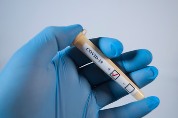 Naklejka premium Blood test with the result of the test for COVID-19 in a hand in a medical glove
