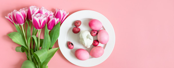 Easter holiday pink table setting with eggs, rabbit and a bouquet of tulips. Banner. Copy space, top view.