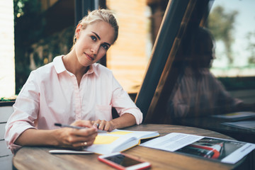 Thoughtful woman taking notes in diary in cafe