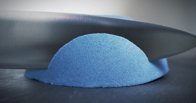 Hemisphere of blue kinetic sand is cut with a large knife. Relaxation techniques. Close-up.