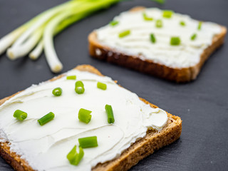 slices of bread with cream cheese spread and fresh 
green onion on black slate breakfast shack concept