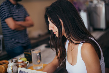 Beautiful young woman sitting at the cafe indoors, reading book, drinking coffee