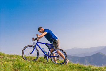 Fototapeta na wymiar Fit male mountain biker pushing his bike uphill while looking exhausted on a sunny summer day.