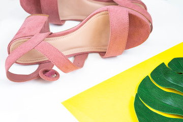 Women's pink summer sandals lie on their sides on a yellow and white background. Fashionable shoes for young girls. Top view. Monstera sheet.
