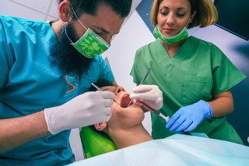 Male dentist with the help of a female dentist examines the mouth and teeth of a teenage boy patient.