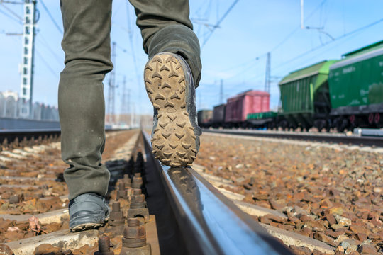 Sole of shoes close-up on rails. Street tramp in dirty jeans walks along the railroad tracks against the background of trains