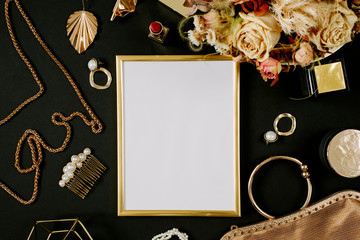 Golden blank frame with luxury golden accessories for women's beauty. Dating concept with red lipstick, dry flowers, golden chain, earrings and handbag on black background. Elegant modern template for