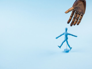Blue wooden human marionette dummy walking alone on monochrome backdrop with big wooden about to take him.