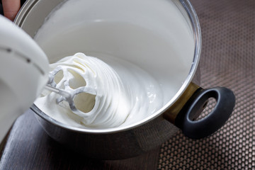 Woman whisking with mixer eggs whites with sugar