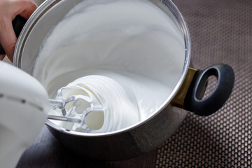 Woman whisking with mixer eggs whites with sugar