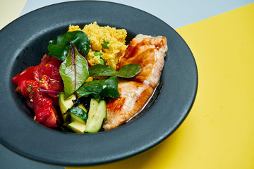Buddha bowl with salmon filet, dried tomatoes, spinach, cucumber and quinoa in a black plate on a colored background. Close up. Suoer food