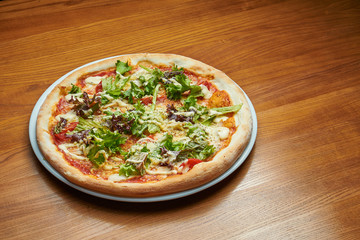 Appetizing baked Italian pizza with cream sauce, lettuce, chicken and parmesan on a white plate on a wooden background. Pizza caesar
