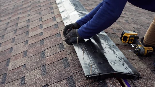 Hands of builder on the roof who is adjusting ridge with screws. Frame house under construction