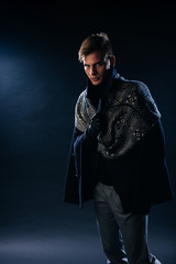 Portrait of a handsome with sharp jawline young man wearing a scarf while posing inside a studio on a black background..