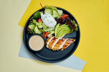 Healthy, dietary food - baked chicken fillet with lettuce and poached egg in a black ceramic plate on colored background. Top view