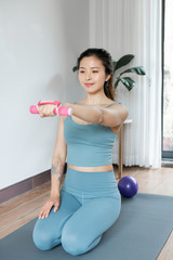 Fototapeta na wymiar A young Asian woman working out with dumbbells by the window