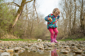 Young girl walking along a shallow stream with rubber pink boots splashing water.