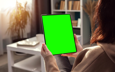 Over shoulder view of woman looking at vertical tablet computer with green screen sitting in flat