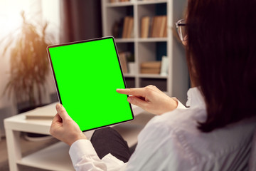 Back view of woman touching tablet green screen sitting in flat over bookcase background