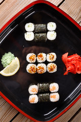 Set of baked sushi rolls with wasabi and ginger on a black background.