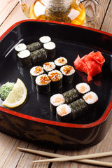 Set of baked sushi rolls with wasabi and ginger on a black background.
