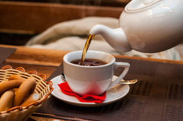 Pouring fresh tea from porcelain tea kettle into white cup. Focus on tea stream, shallow depth of...